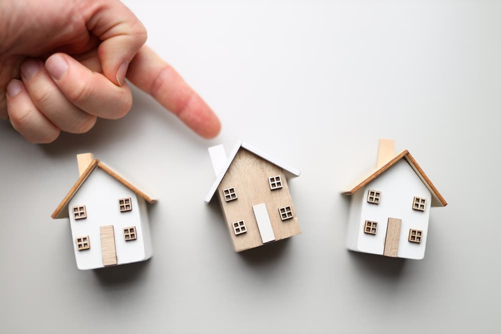 Hand,Pointing,At,Miniature,House,Models,On,White,Background.
